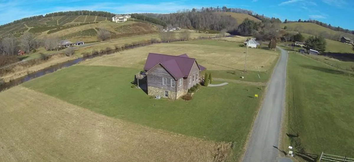 An exterior view of the house set against a backdrop of rolling hills, a nearby road, and a vineyard. The broad landscape captures the sense of open space and the promise of nearby trails and adventures.