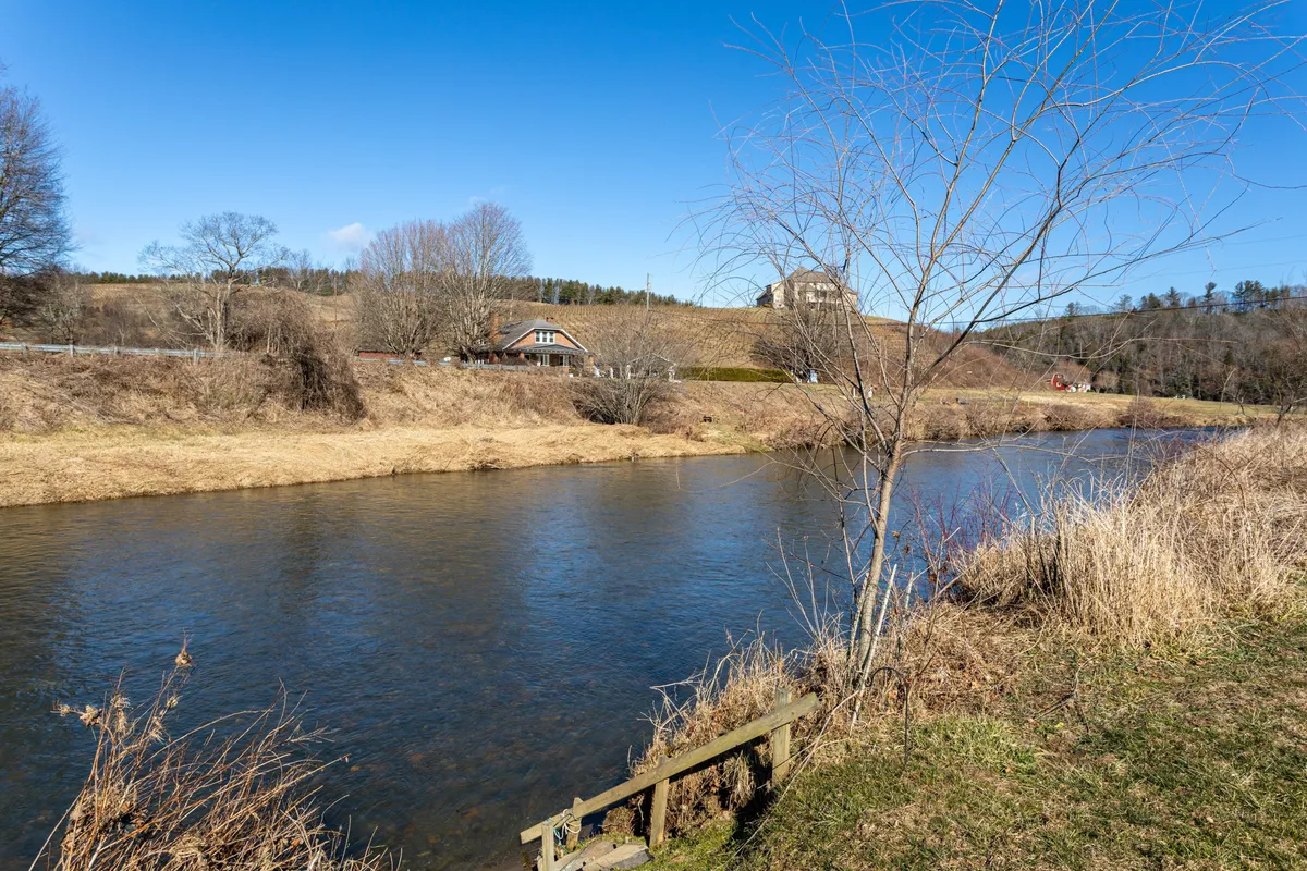 A tranquil river scene with open grassland, houses in the distance, and bare trees lining the banks. Activities like fishing, picnicking, and birdwatching are suggested by the peaceful setting, which highlights the riverfront access and opportunities for water-based fun.