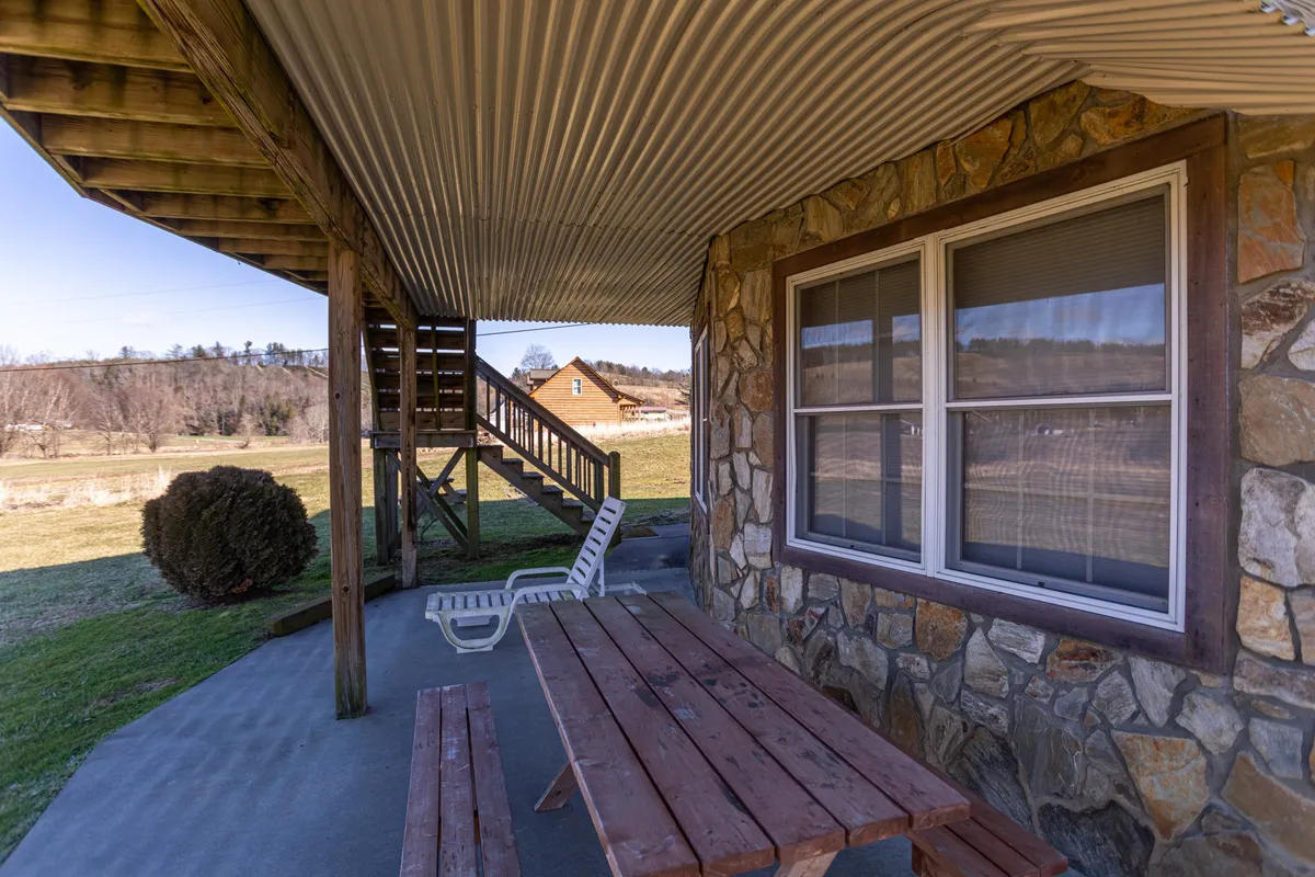 The image shows a casual outdoor space with a stone wall, a wooden picnic table, a white lounge chair, and stairs leading up to the house. The area is positioned to maximize enjoyment of the view and direct access to the outdoors—ideal for relaxing after a day of hiking or paddling.
