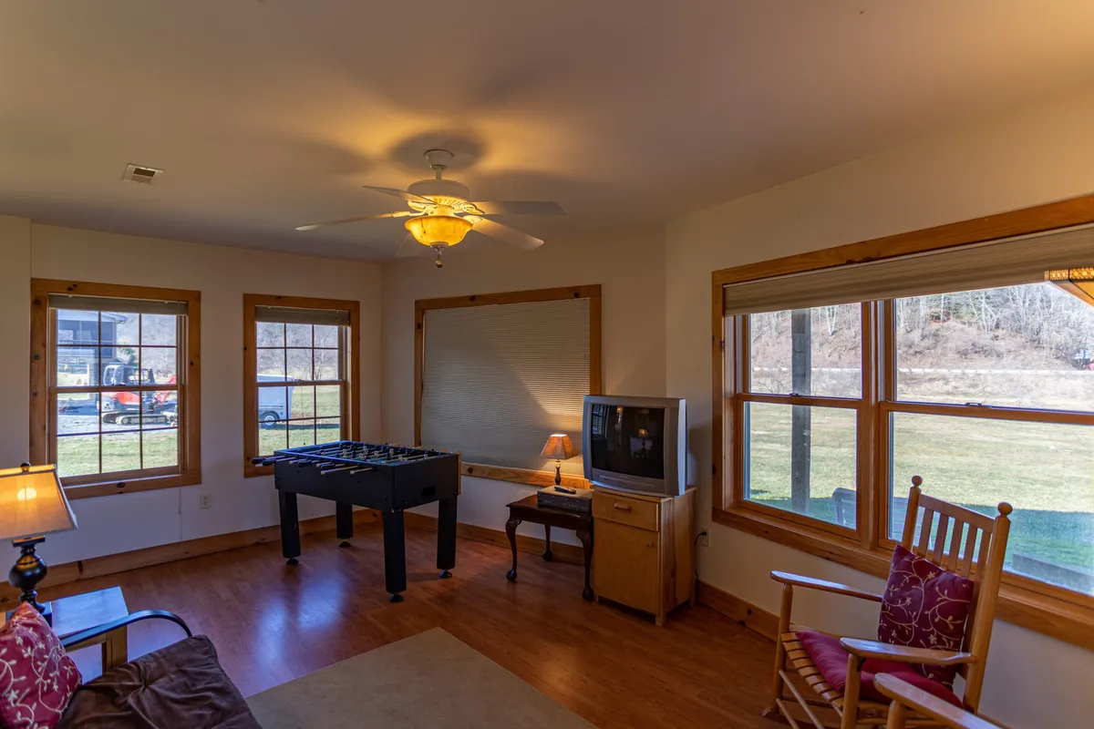 A lower-level room featuring a foosball table, a rocking chair angled towards a window with outdoor views, and a cozy seating arrangement. The space is bright and casual, perfect for relaxing, playing games, or unwinding while still feeling connected to the outdoors.