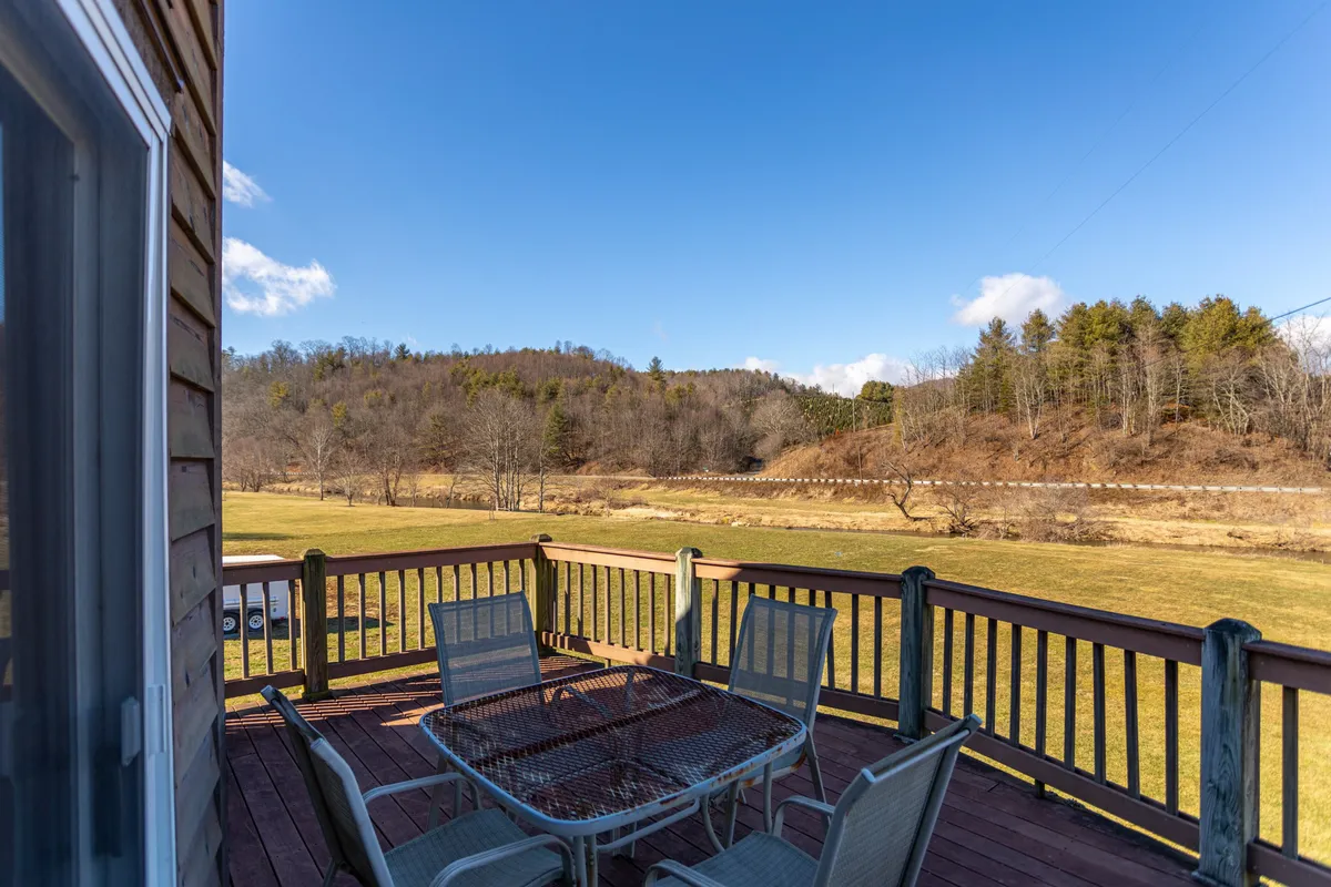 A scenic deck furnished with a table and chairs, offering an expansive view over the surrounding landscape and tree-dotted hillsides. The setting is ideal for outdoor dining, family gatherings, or simply soaking up sunsets and stargazing.